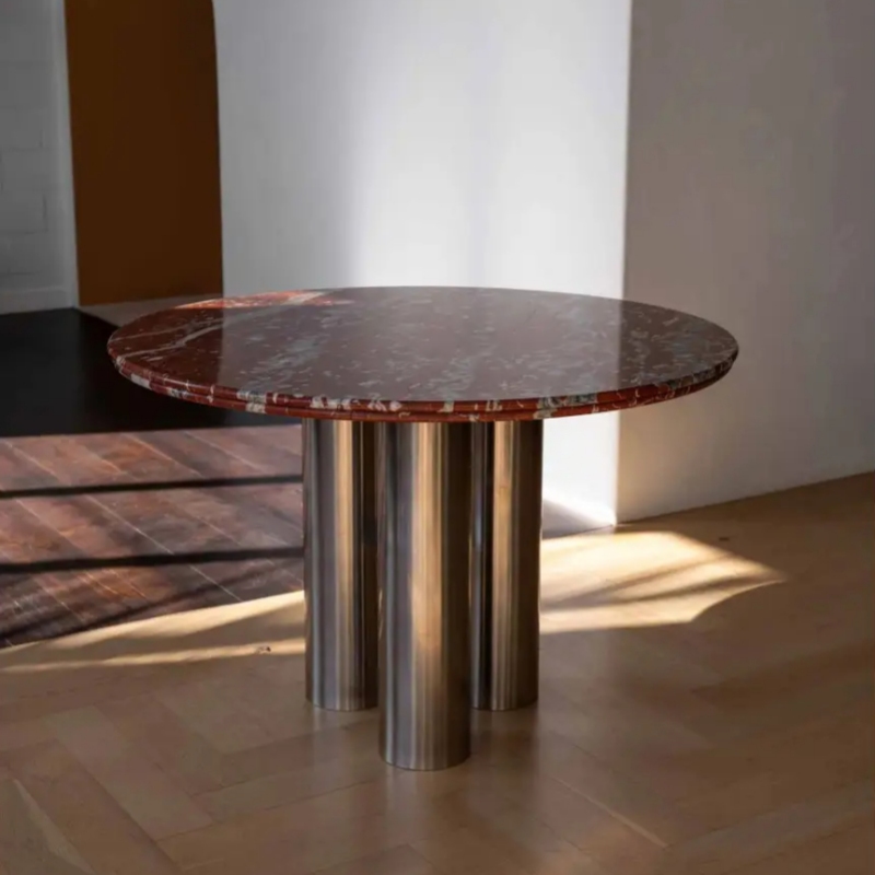 Red veined marble round table with polished stainless steel cylindrical bases - lit by natural sunlight in modern interior